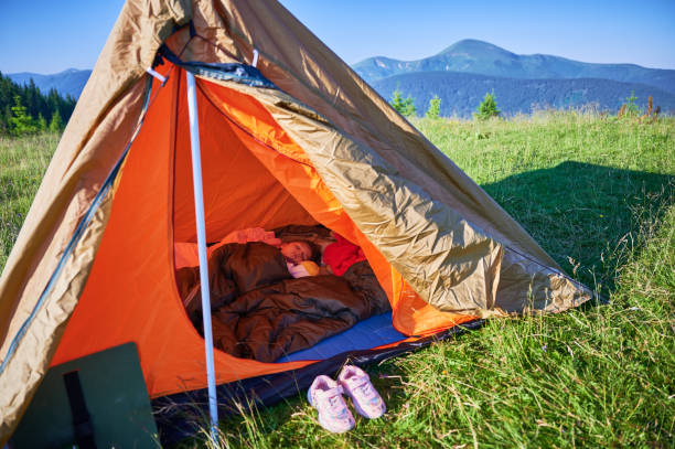 istock Child sleeping peacefully inside orange and brown tent, snug in sleeping bag on blue mat. 2199486359