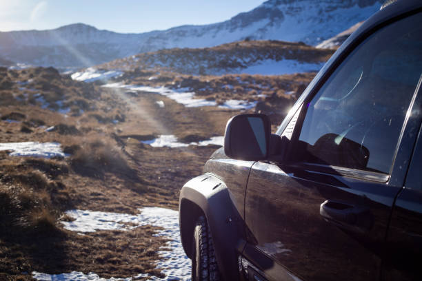 Rugged off-road vehicle parked by a snow-covered roadside. Ice and dirt coat the front bumper, icicles hang from the undercarriage, and snow clings to the tire, highlighting harsh winter conditions.