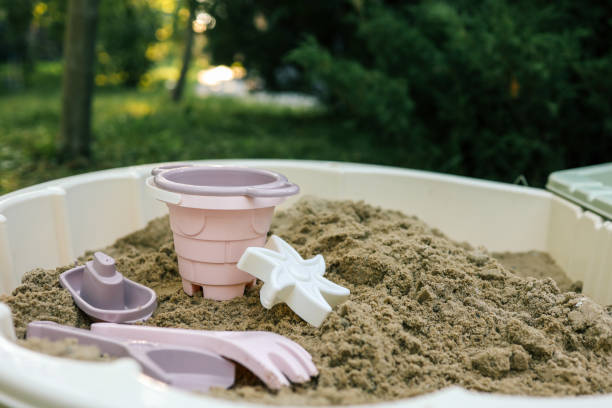istock Plastic sandbox toys, including a bucket, sieve, rake, and boat, arranged in a backyard sandbox. Soft pastel colors contrast with natural greenery, creating a playful and serene outdoor setting 2199488804