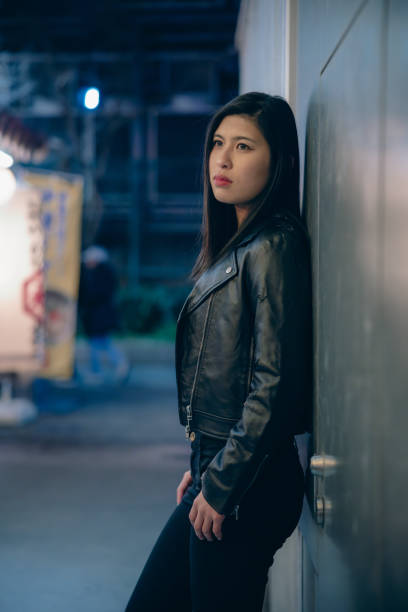 Young woman in leather jacket leaning on wall at night