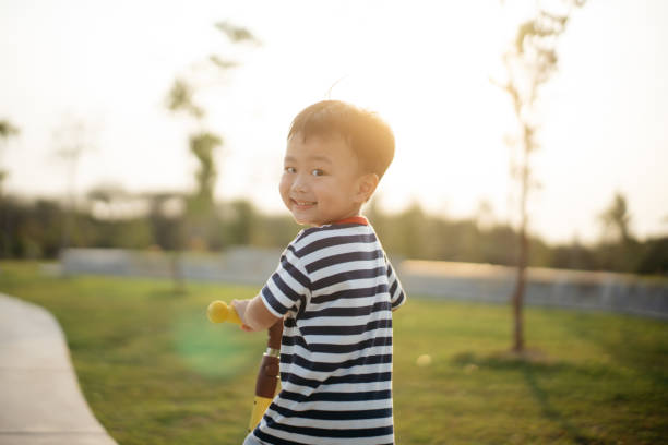 Adorable boy looking at camera while enjoys riding on scooter at public park