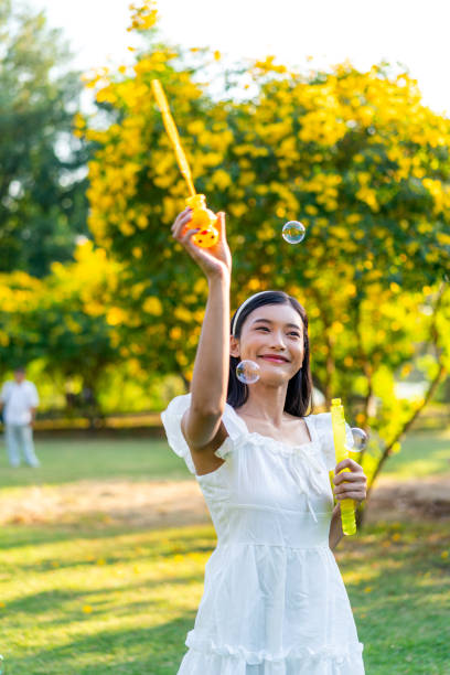 istock Young Asian Woman Blowing Bubbles Outdoors in a Park on a Sunny Day 2199505728