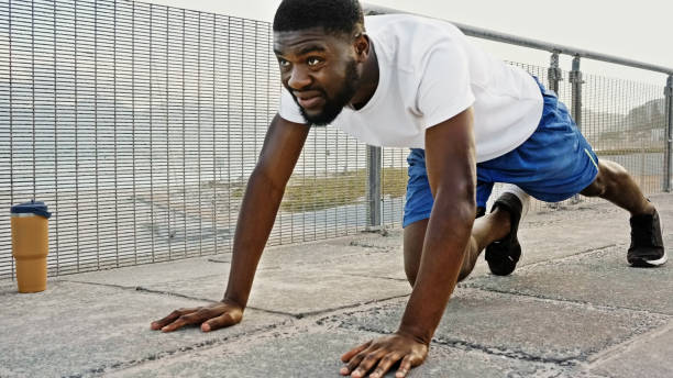 Young fit African man doing mountain climbers exercises during his morning workout on a concrete road along the sea