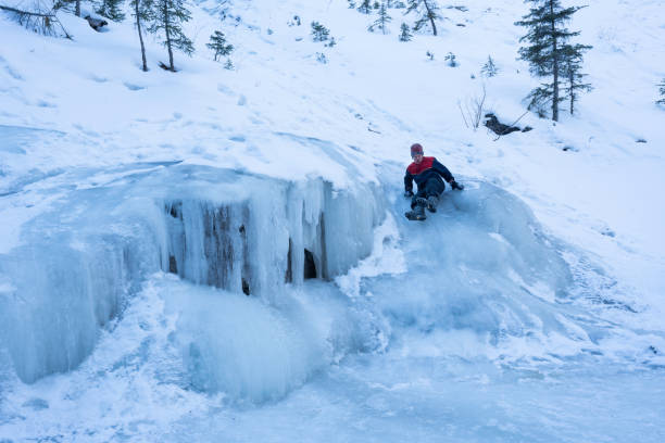 Jasper, Canada - March 21, 2023: Male tourist slides down ice at Maligne canyon, Jasper National Park, Alberta