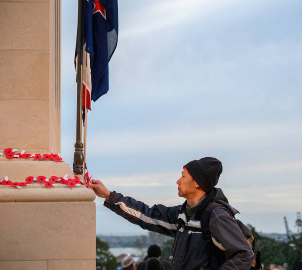 Man placing red poppies on the wall. Anzac Day commemoration. Auckland. Vertical format.