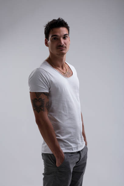 istock Young man with tattoos posing in studio with hands in pockets 2199528982