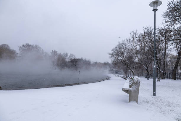 istock Snow-covered benches in a park beside a lake 2199530054