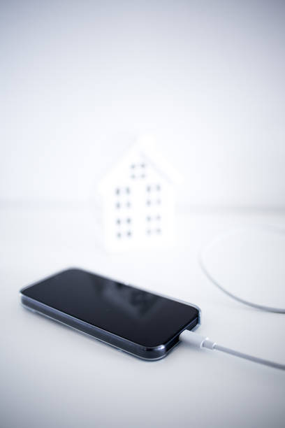 Smartphone charging by miniature house on white background.