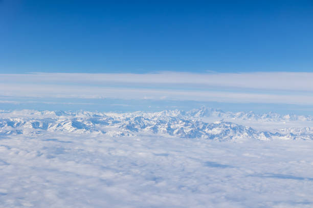 Amazing view of the European Alps from the airplane window, in winter time. Snowy peaks emerging from the clouds.
