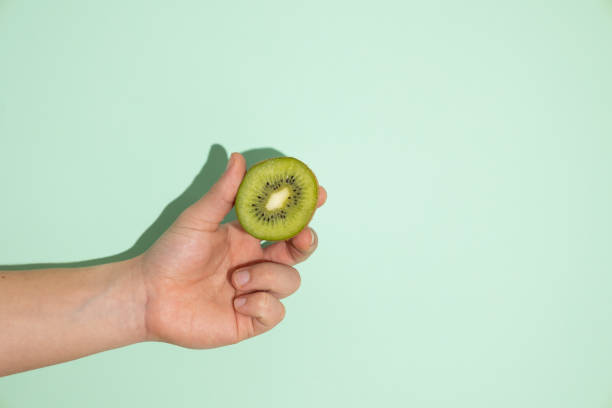 istock Male hand holding a kiwi on a light green background 2199543131