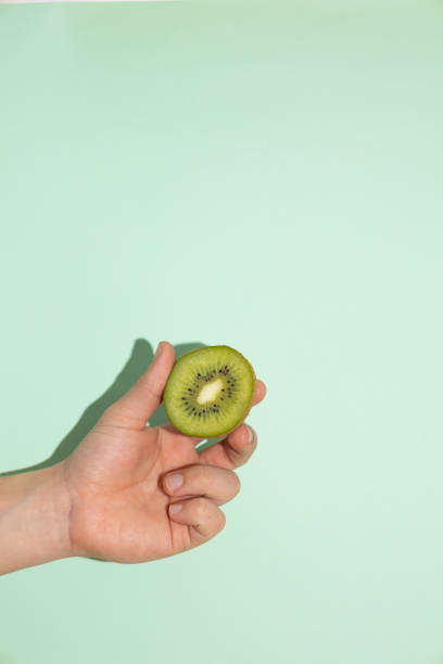 istock Vertical image of male hand holding a kiwi on a light green background 2199543135