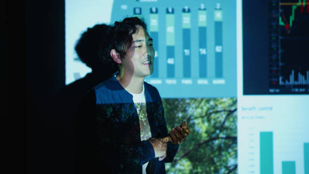 A young businessman gives a presentation on sustainability metrics in a dimly lit office, emphasizing green initiatives and eco-friendly growth. The projected slides highlight environmental data, with graphs and images of greenery reinforcing the company's commitment to sustainability.