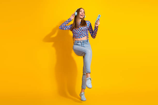 istock Young woman dancing to music while holding smartphone with yellow backdrop 2199555404