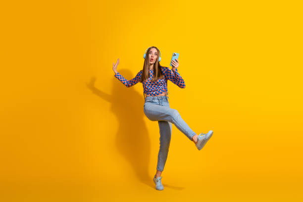 istock Girl Expressing Joy with Smartphone on Vibrant Yellow Backdrop for Advertising 2199555412