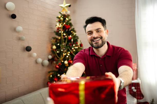 istock Man giving Christmas present to someone near Christmas tree 2199557399