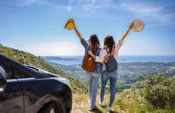 Two young adults embrace and raise hats, celebrating a scenic view overlooking Dubrovnik