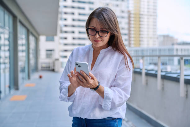 istock Mature woman using smartphone, modern city background 2199565269