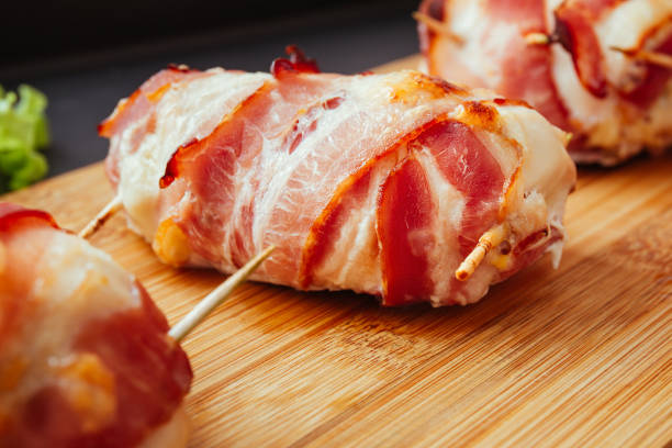 istock Baked chicken wrapped in bacon. Delicious appetizer with crispy smoked bacon. Chicken breast wrapped in bacon on wooden board. Dark black background, top view. 2199568380