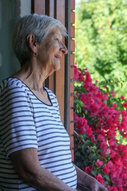 portrait of senior latino woman looking at her garden from the window contemplating