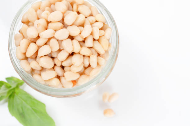 Bowl filled with shelled pine nuts with scattered nuts on white background