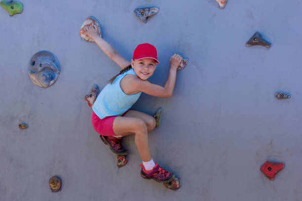 A young woman climbs an outdoor rock wall with focused determination, showcasing her active lifestyle and tenacity. Her hands grip firmly, highlighting the strength and effort involved in rock climbing.