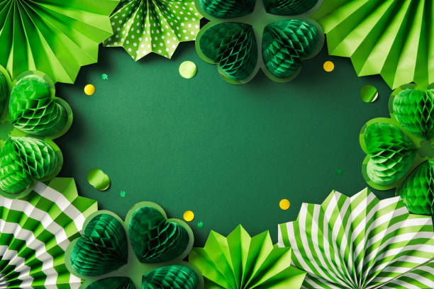 istock Happy St Patrick's Day greeting card design. Festive green paper decorations, including shamrocks and fans, arranged in a border on a green background with scattered yellow and green confetti 2199584005