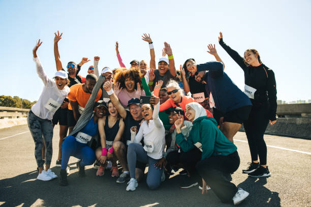 A diverse and joyful group of people gathers for a selfie after finishing a 5km race on a sunny day. The image captures the spirit and energy of fitness, health, and community engagement outdoors.