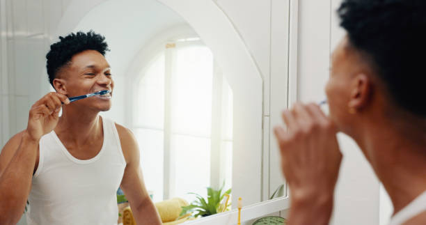 istock Bathroom, house and man brushing teeth, reflection and hygiene with morning routine. Person, mirror and grooming with toothbrush, fresh breath or cleaning mouth with dental health, smile or whitening 2199585565