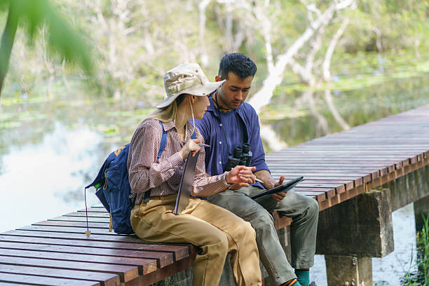 University biology and botany students are exploring and collecting data within a peatland for research using binoculars and taking notes.