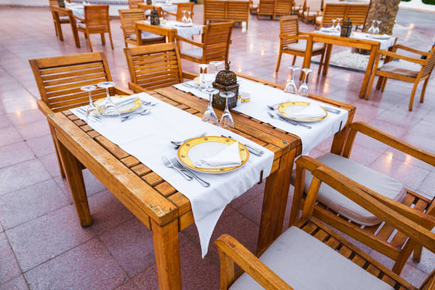 Rustic wooden tables are elegantly arranged with fine tableware, surrounded by a tranquil outdoor setting, capturing the essence of a cozy dining experience during sunset.