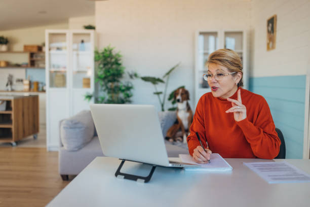 istock Senior adult woman watching web training, online webinar on laptop computer remote working or e-learning class from home office, video calling having virtual meeting, writing notes 2199598480