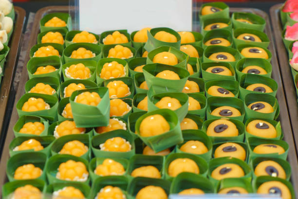 close-up shot of traditional Thai golden sweets made from egg yolks and sugar, elegantly presented in small banana leaf cups. These bite-sized confections showcase the intricate shapes, bright color, and rich flavor that make them popular at festive occasions and street markets alike.