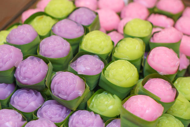 close-up shot of delicate, rose-shaped Thai jelly desserts in soft pastel hues—pink, green, and purple—neatly wrapped in small banana leaf cups.