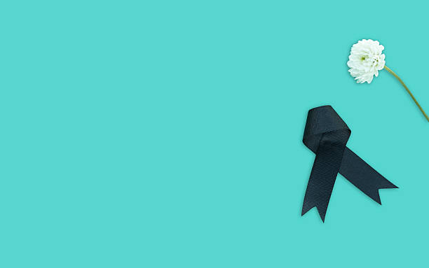 istock Black funeral ribbon and white flower on blue background. Space for text 2199600909