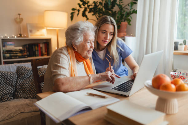 istock Social worker helping elderly lady with managing her finances, teaching her to use online banking on laptop. 2199605448