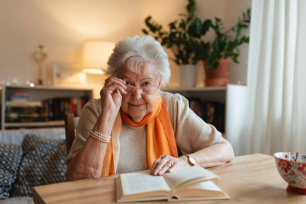 istock Side view of elderly lady reading a book, sitting at the kitchen table and sipping tea. 2199605816