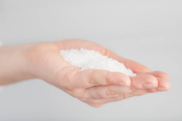 Hand is holding salt crystals to camera in front of white background.