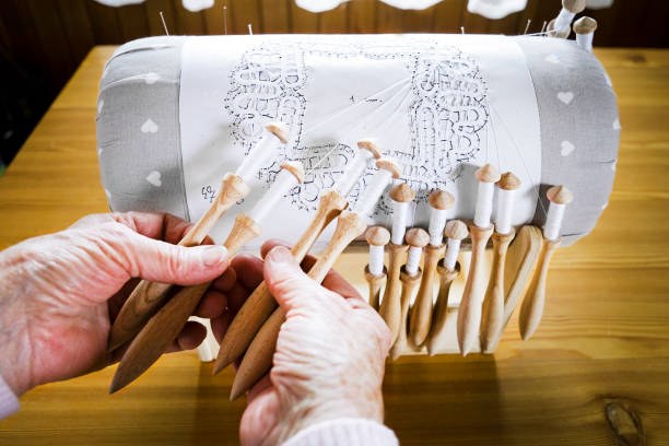 Making bobbin lace in traditional way. Detail on hands holding wooden bobbins with wound thread. Pillow lace.