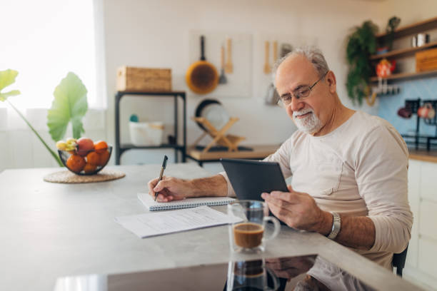 istock Senior man with eyeglasses uses his digital tablet for further education through e-learning. He sits comfortably at home, taking advantage of technology to improve his knowledge 2199623615