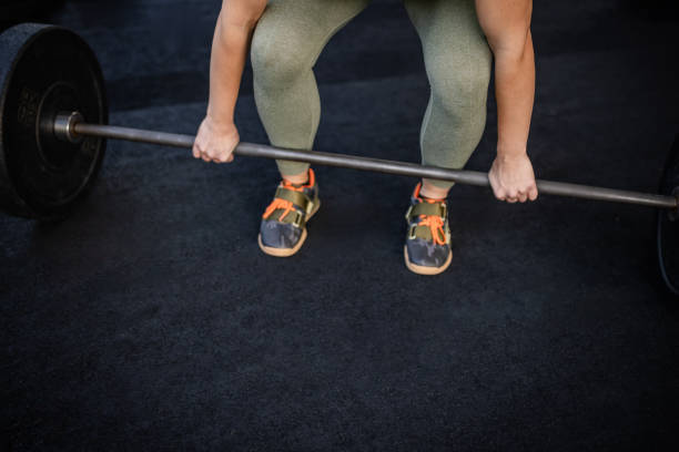 An adult athlete trains in a gym, gripping a barbell and preparing for a deadlift. The environment reflects dedication to health and wellbeing, emphasizing strength and fitness.