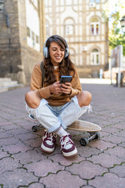 istock Young female skater sitting on skateboard and using phone 2199631230