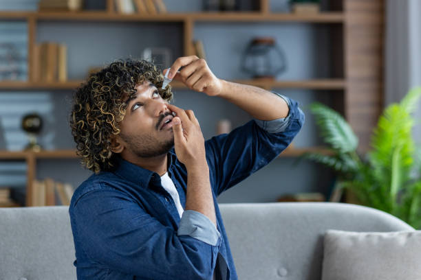 istock Tired man sitting on the couch at home, putting eye drops in his eyes from overwork from working on the computer, in the living room on the couch 2199633499