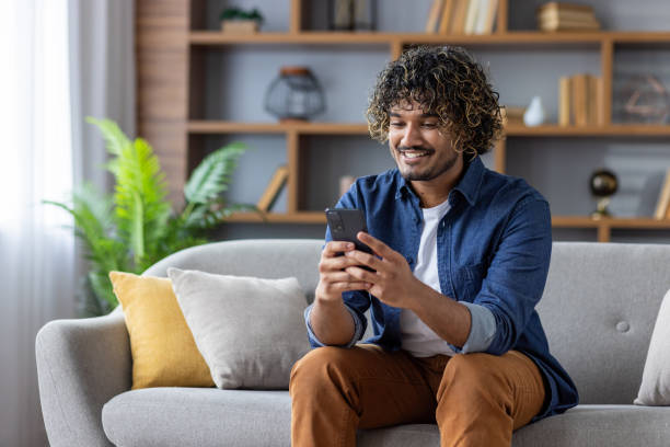 istock Smiling man using smartphone on couch enjoying a relaxed moment at home 2199633506