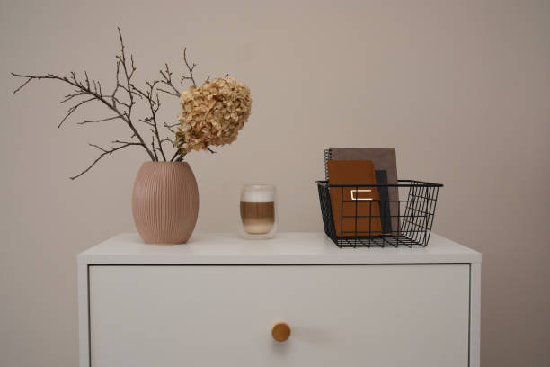 Modern Minimalist Decor of dried Flowers and branches in ceramic vase, drink coffee, notebooks in basket on white table. High quality photo