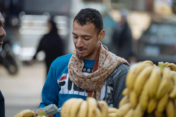 Giza, Egypt - January 23, 2025: Day at the local groceries market on the streets of Giza, famous for historic landmarks - Giza Pyramids. Cheerful fruit salesman attracting customers with the smile.