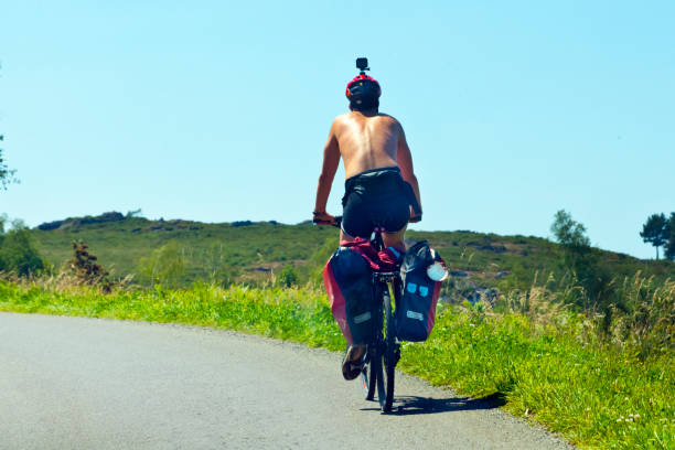 Rear view of pilgrim cyclist riding along the 'camino de Santiago', camera on his helmet, scallop symbol. The camino de Santiago is an ancient pilgrimage route in Europe which belongs to the UNESCO world heritage.
