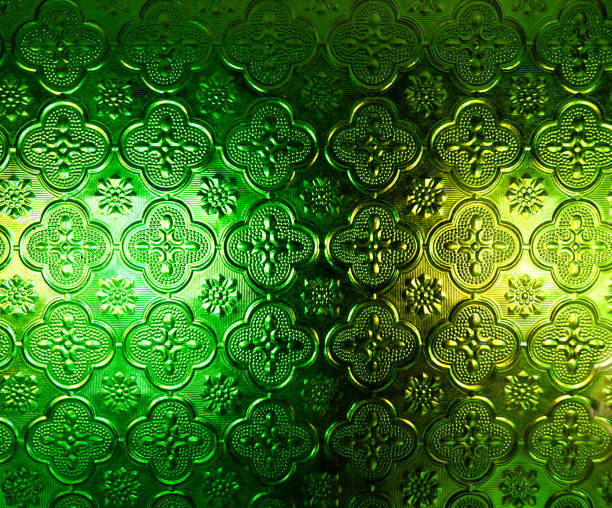 Background of light reflected from behind green opaque glass with delicate etched floral design pattern. Frosted window pane surface with back lit. Close up.