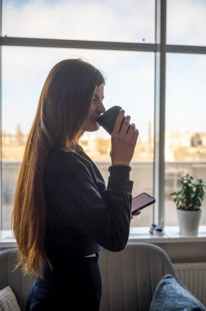 istock a slender girl stands in front of the window and drinks a drink from a plastic cup 2199656795