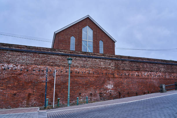 This is a photo of a building with an impressive red brick wall and white door. Although it has a simple appearance, the texture of the brick and the presence of the door catch the eye. The composition of a part of a building can also be used as an abstract background material, and is a stock photo that fits themes such as architecture, history, simplicity, and materials.