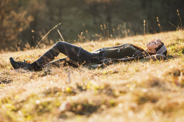 Cute smiling young woman is lying down on the ground in early spring sunny day and enjoying calm.